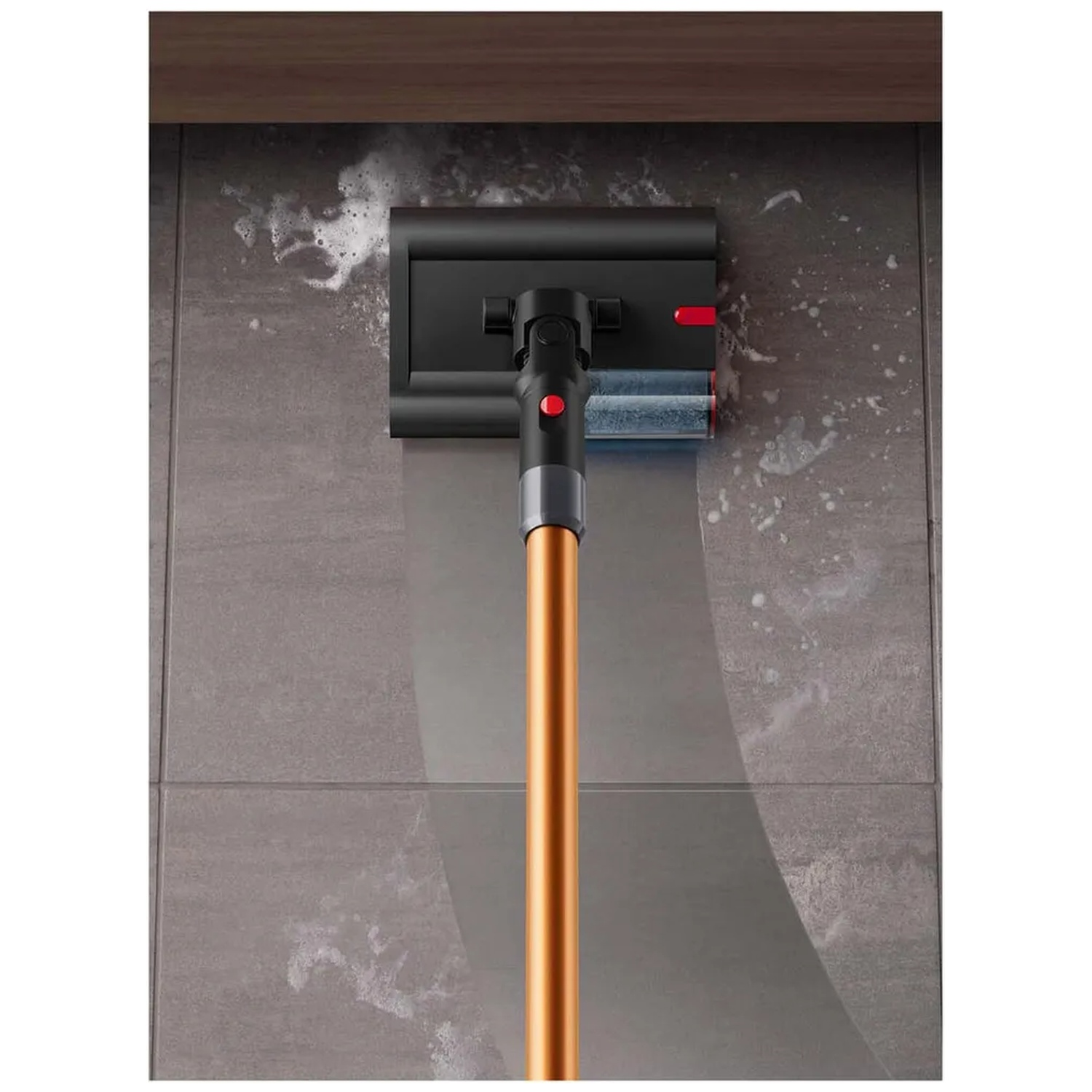Une tête d'aspirateur avec brosses nettoie un mur carrelé avec de la mousse de savon.