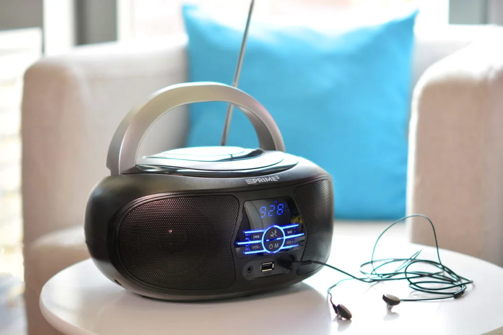 Czarna wieża z słuchawkami na białym stole, niebieska poduszka w tle.