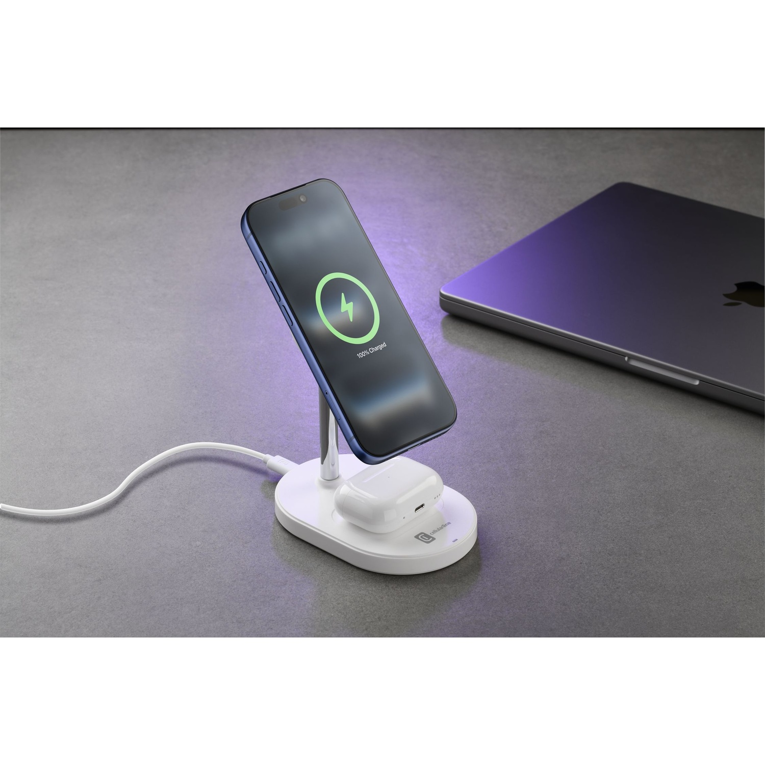 Un caricatore wireless bianco tiene un telefono e auricolari. Un laptop è nelle vicinanze.