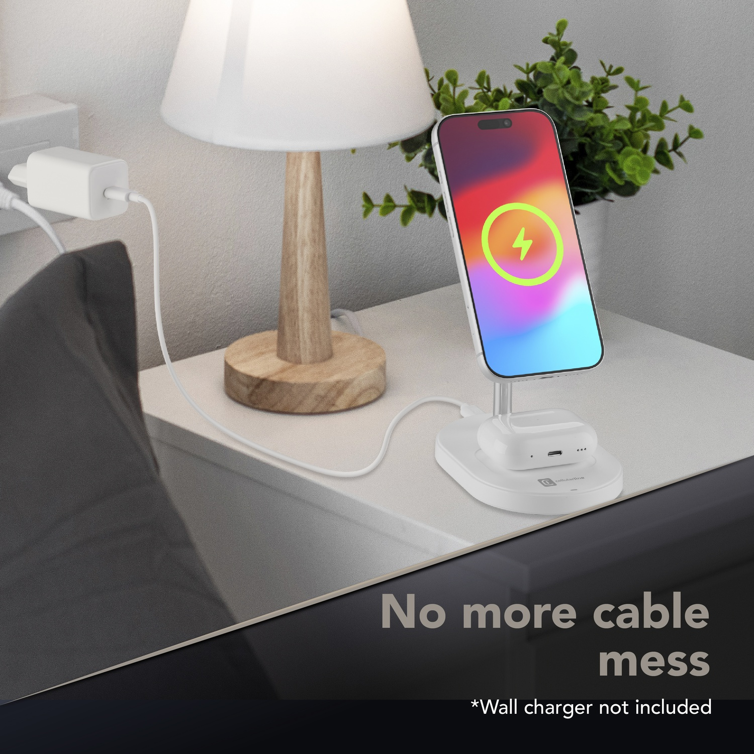 Un caricabatterie wireless bianco tiene un telefono e auricolari su un comodino accanto a una lampada.