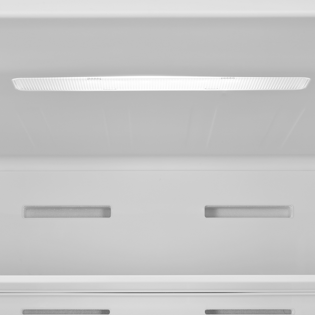 Ein heller, rechteckiger Lichtstreifen oben in einem weißen Innenraum. Darunter zwei schmale, horizontale Lüftungsschlitze.