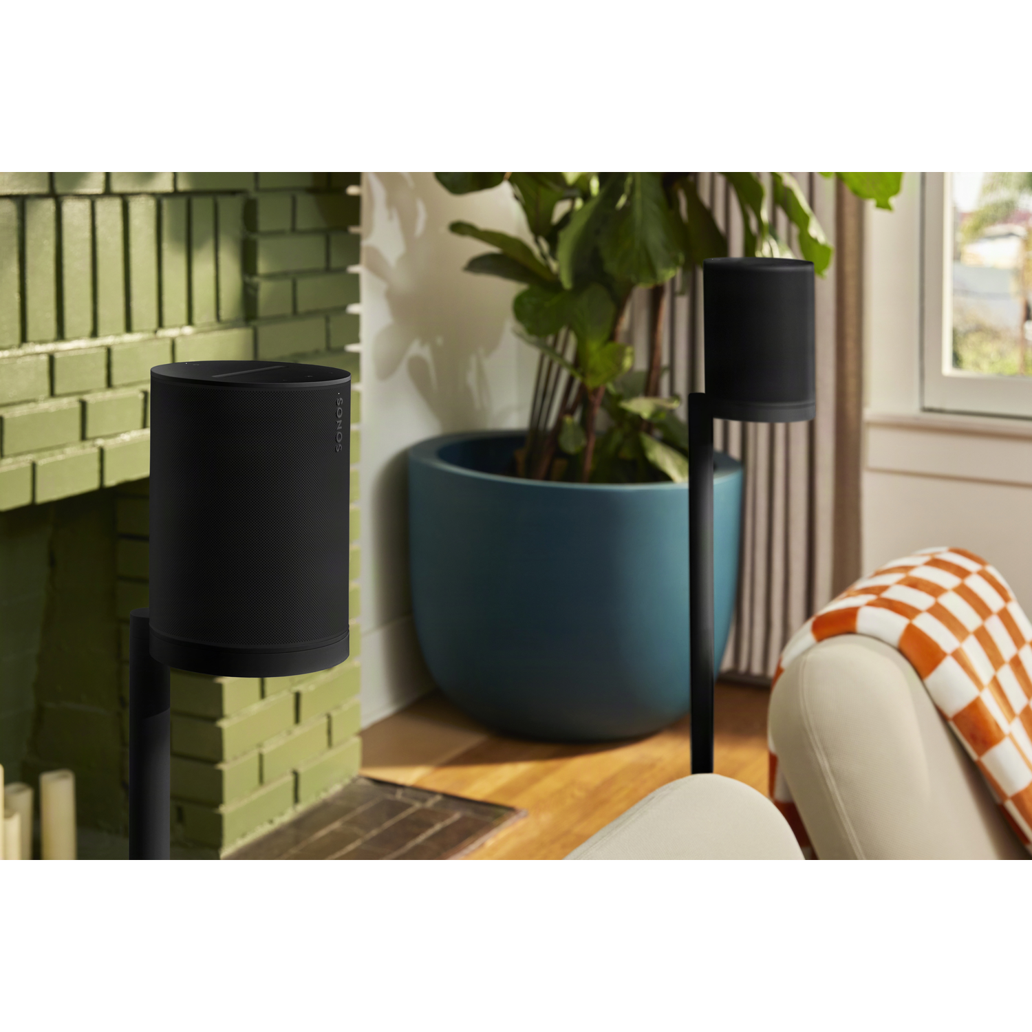 Twee zwarte luidsprekers op standaards voor een open haard, pot en fauteuil.