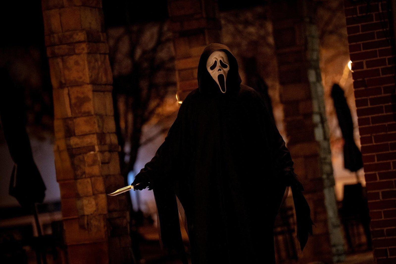 Eine Person mit Ghostface-Maske und schwarzem Umhang hält ein Messer.