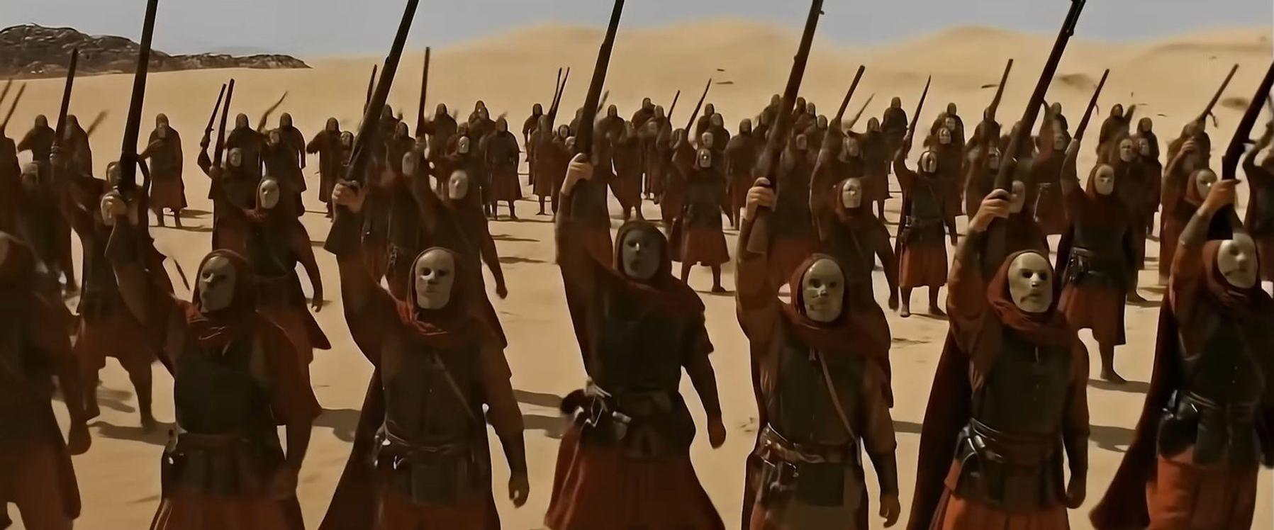 Eine Armee in roten Roben und weißen Masken hebt Waffen in der Wüste.