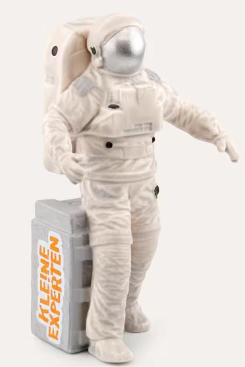Ein Astronaut-Spielzeug in einem weißen Anzug steht neben einer grauen Kiste mit orangener Schrift.