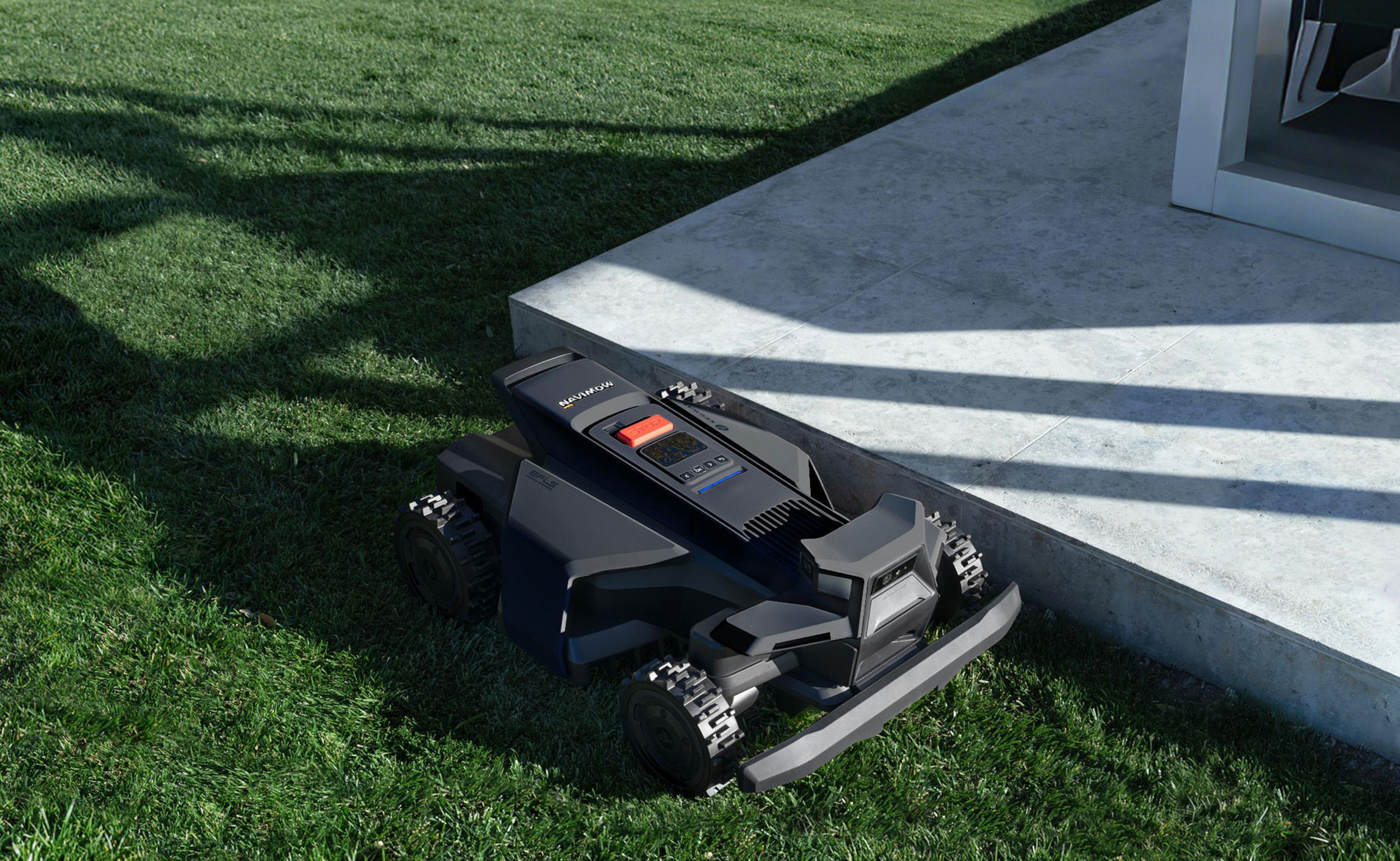 Ein schwarzer Mähroboter auf einem grünen Rasen neben einer Betonplatte.