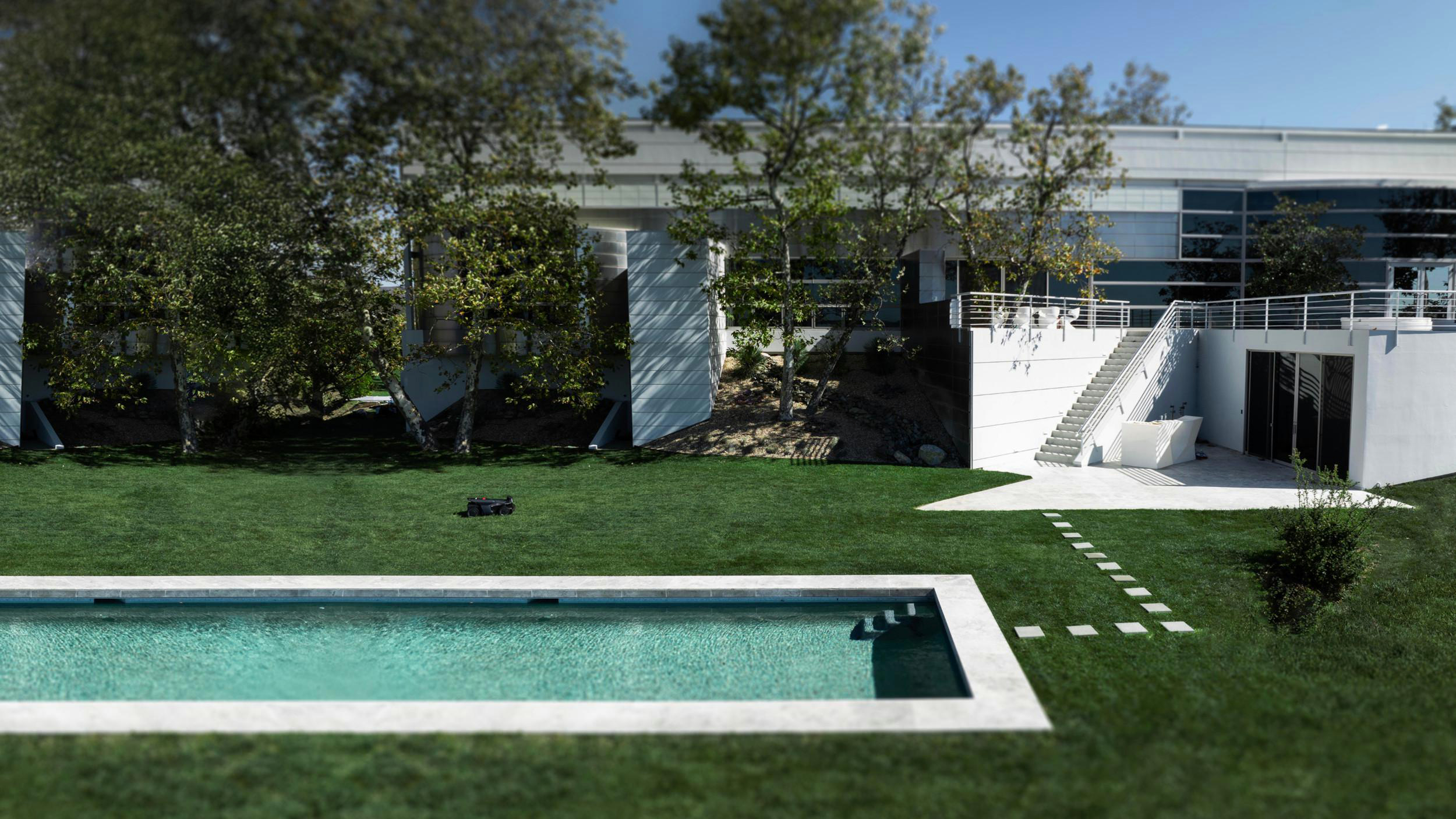 Ein modernes Haus mit Pool und Rasen. Ein Mähroboter steht auf dem Rasen.
