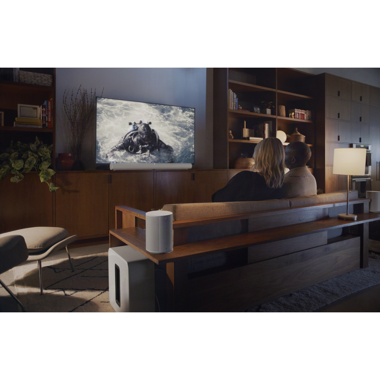 Een stel kijkt tv in een woonkamer met soundbar en subwoofer.