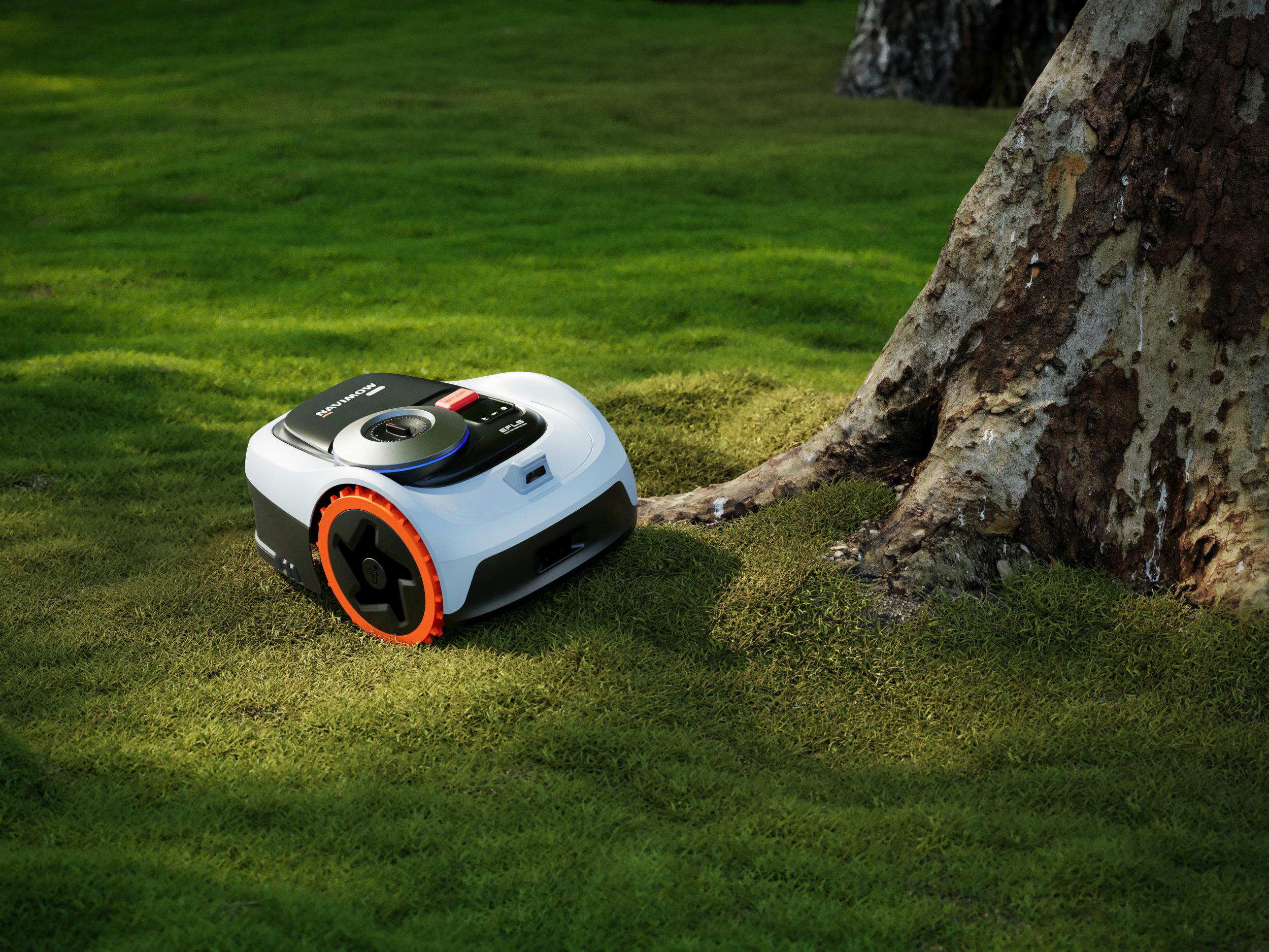 Ein weißer Mähroboter mit orangefarbenen Rädern steht auf einem grünen Rasen neben einem Baum.
