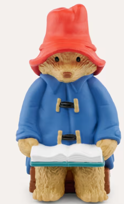Paddington Bär in blauer Jacke, rotem Hut und mit Buch.