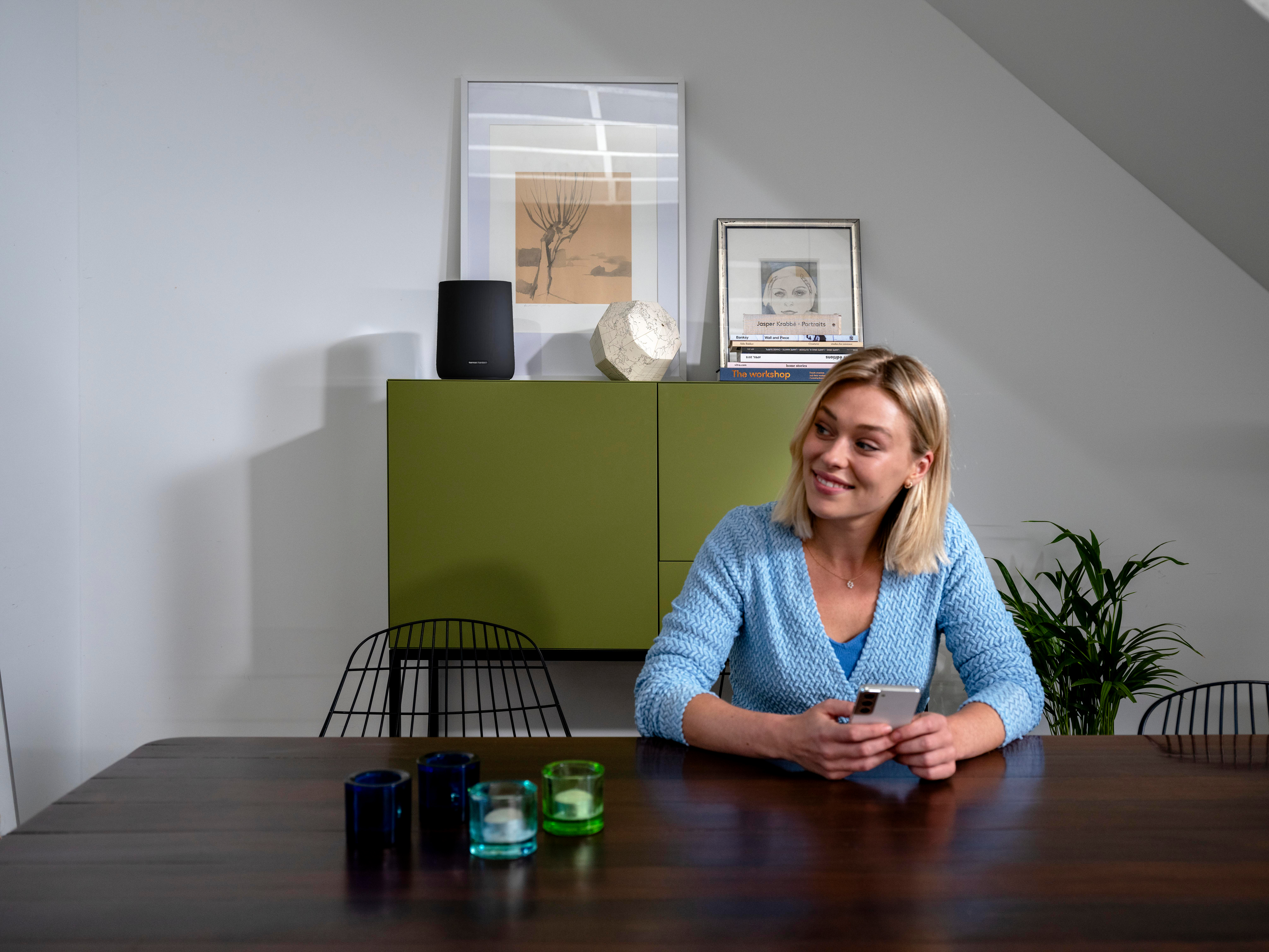 Eine Frau sitzt an einem Holztisch und hält ein Smartphone.