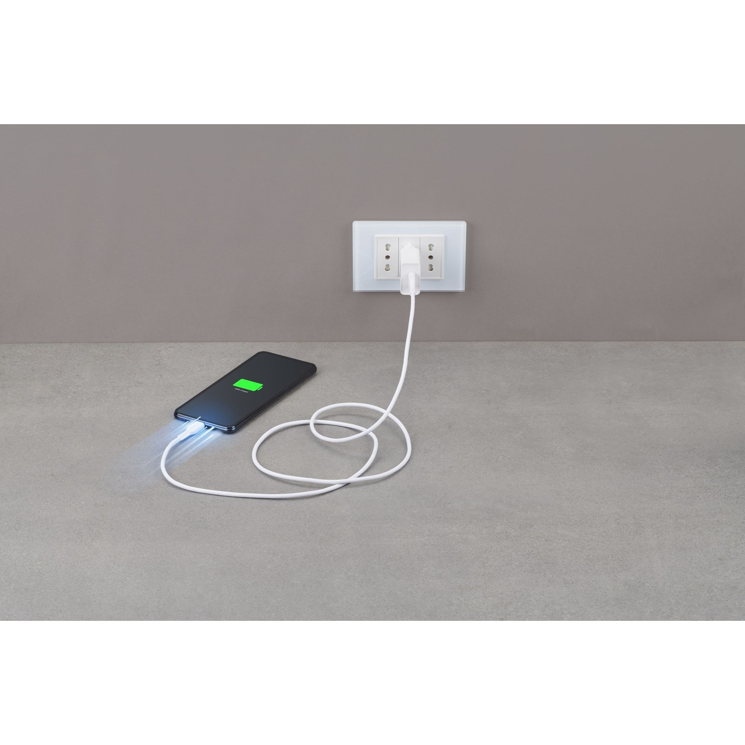 Uno smartphone è collegato a una presa a muro tramite un cavo bianco.