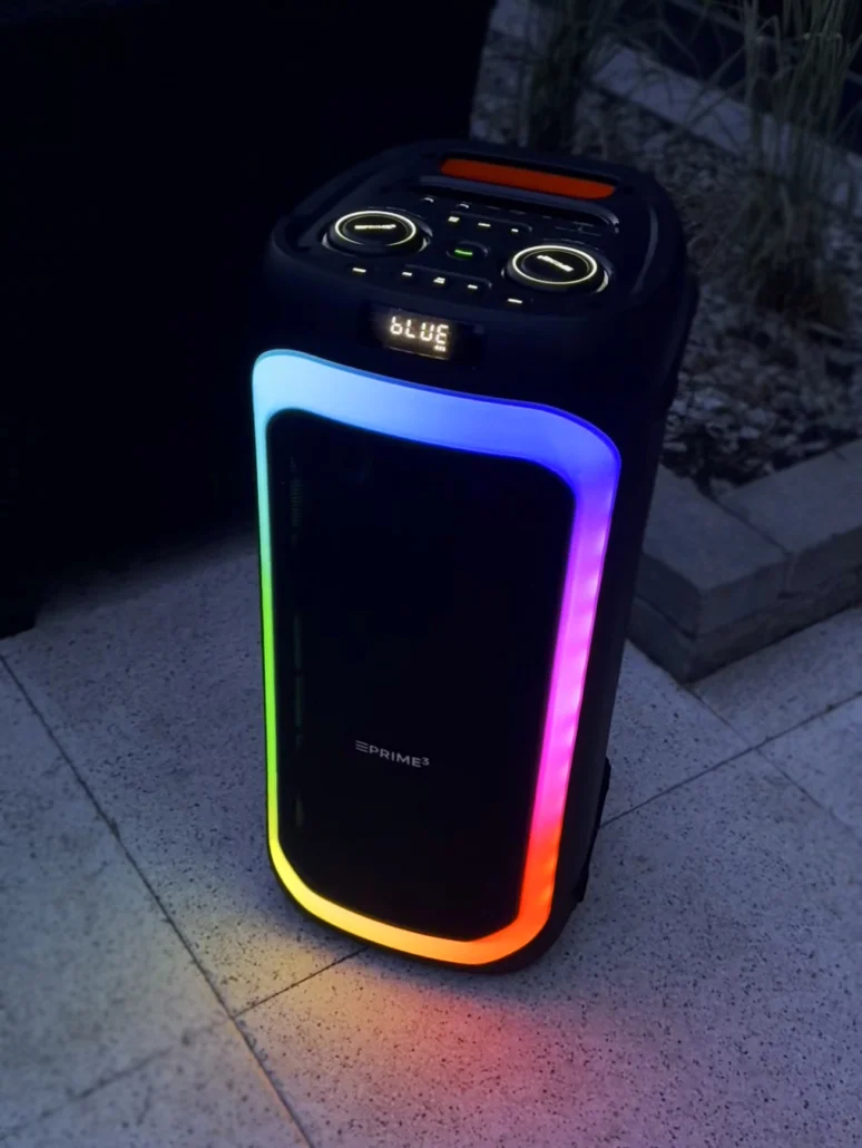 Czarny głośnik z kolorowym podświetleniem LED stoi na kamiennym patio.