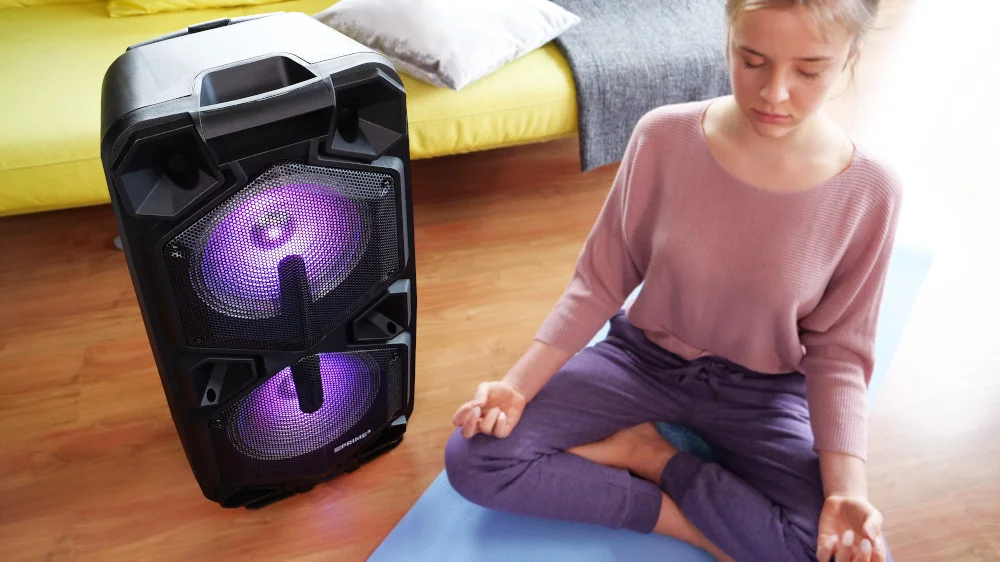 Młoda kobieta medytuje w pozycji lotosu obok dużego czarnego głośnika z fioletowymi światłami.