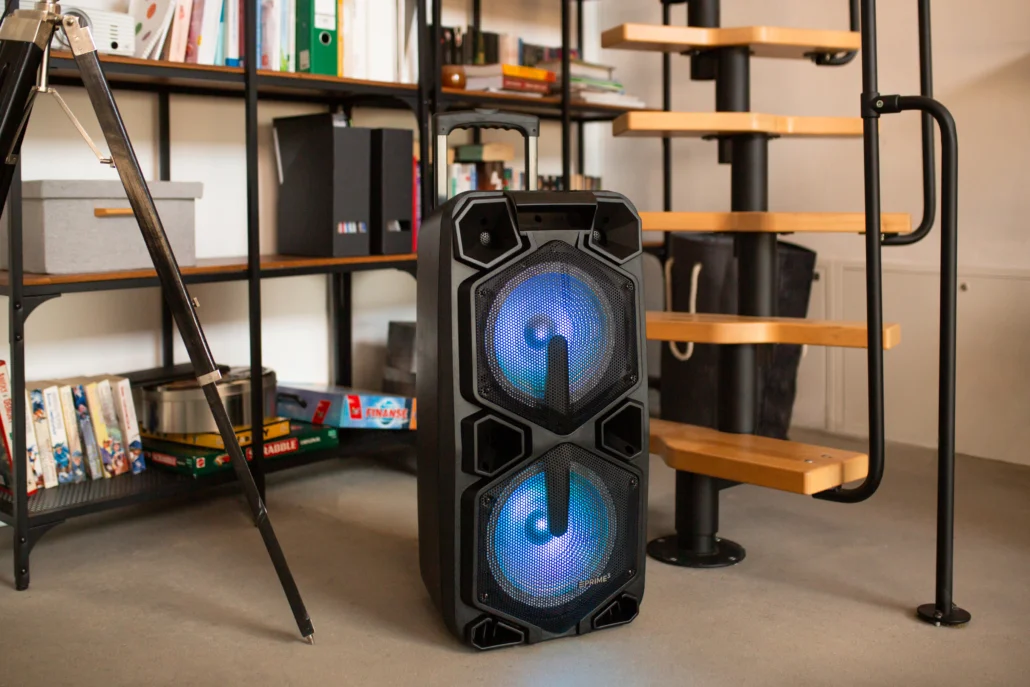 Duży czarny głośnik z niebieskimi światłami stoi na podłodze obok schodów kręconych.