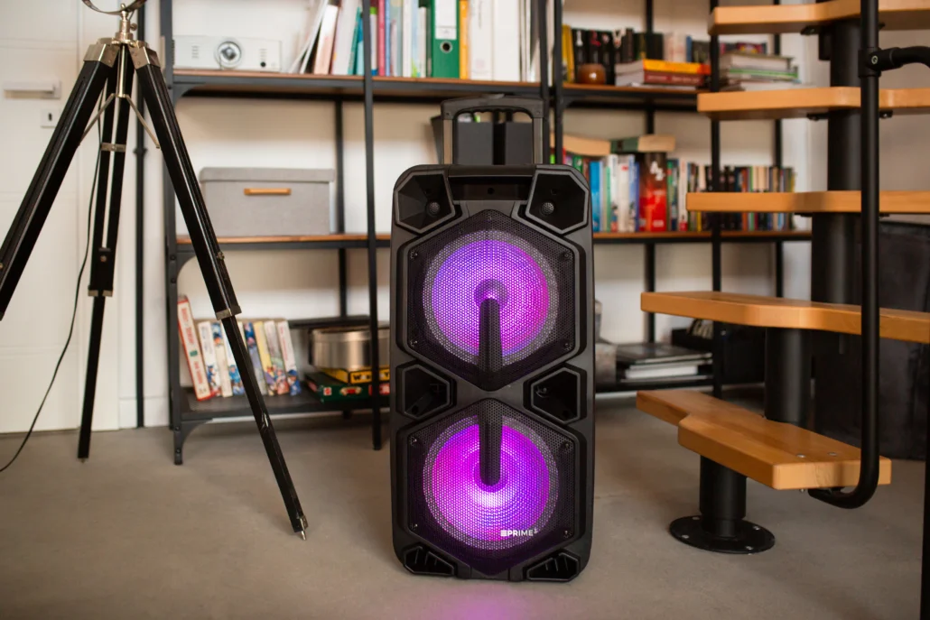Duży czarny głośnik z fioletowymi światłami stoi na szarej podłodze.