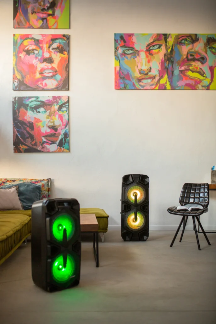 Dwa głośniki ze światłami stoją w pokoju z kolorową sztuką na ścianie.