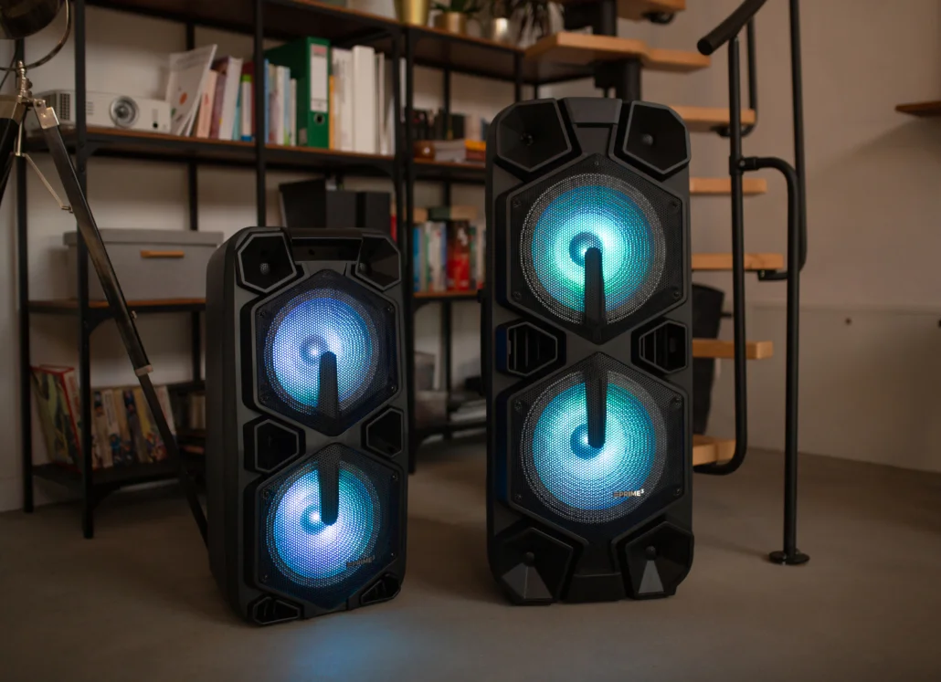 Dwa czarne głośniki z niebieskimi światłami, półki w tle.
