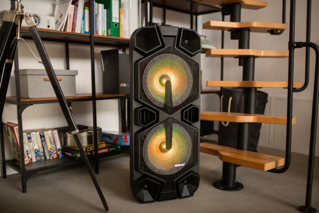 Duży czarny głośnik z podświetlanymi przetwornikami stoi w pokoju.