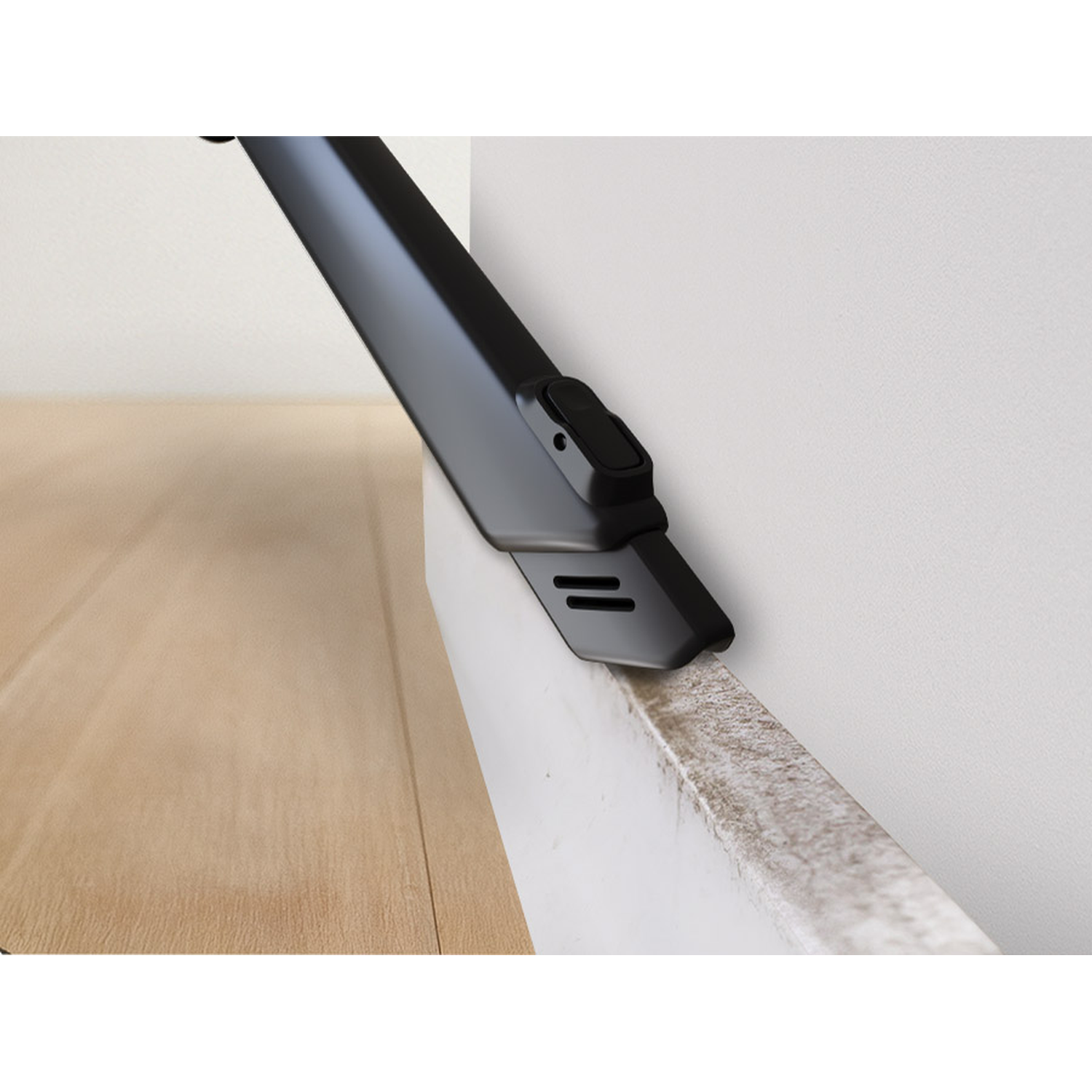 A black vacuum attachment cleans a dirty white baseboard next to a wood floor.