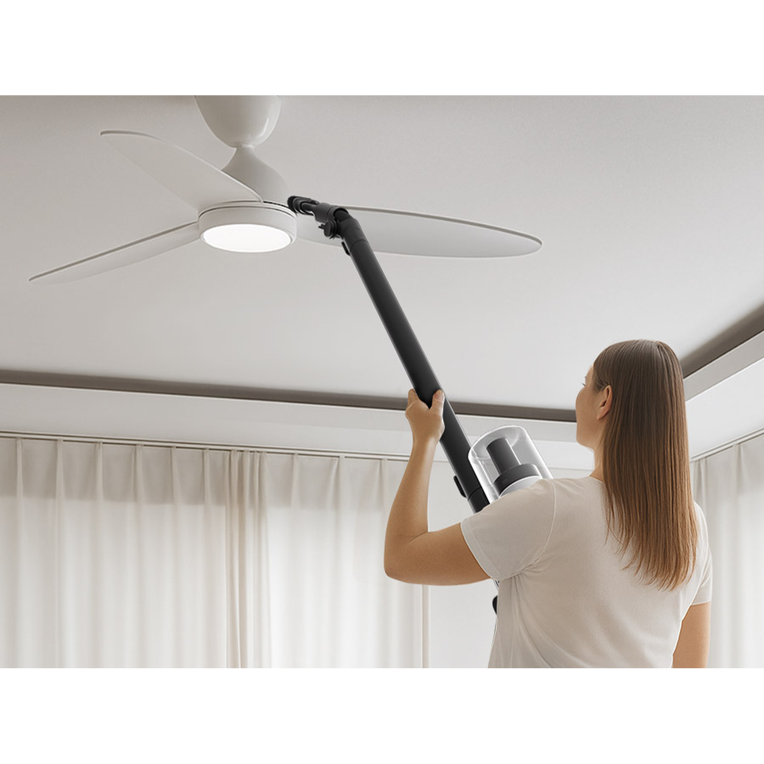 A woman vacuums a ceiling fan with a handheld vacuum cleaner.