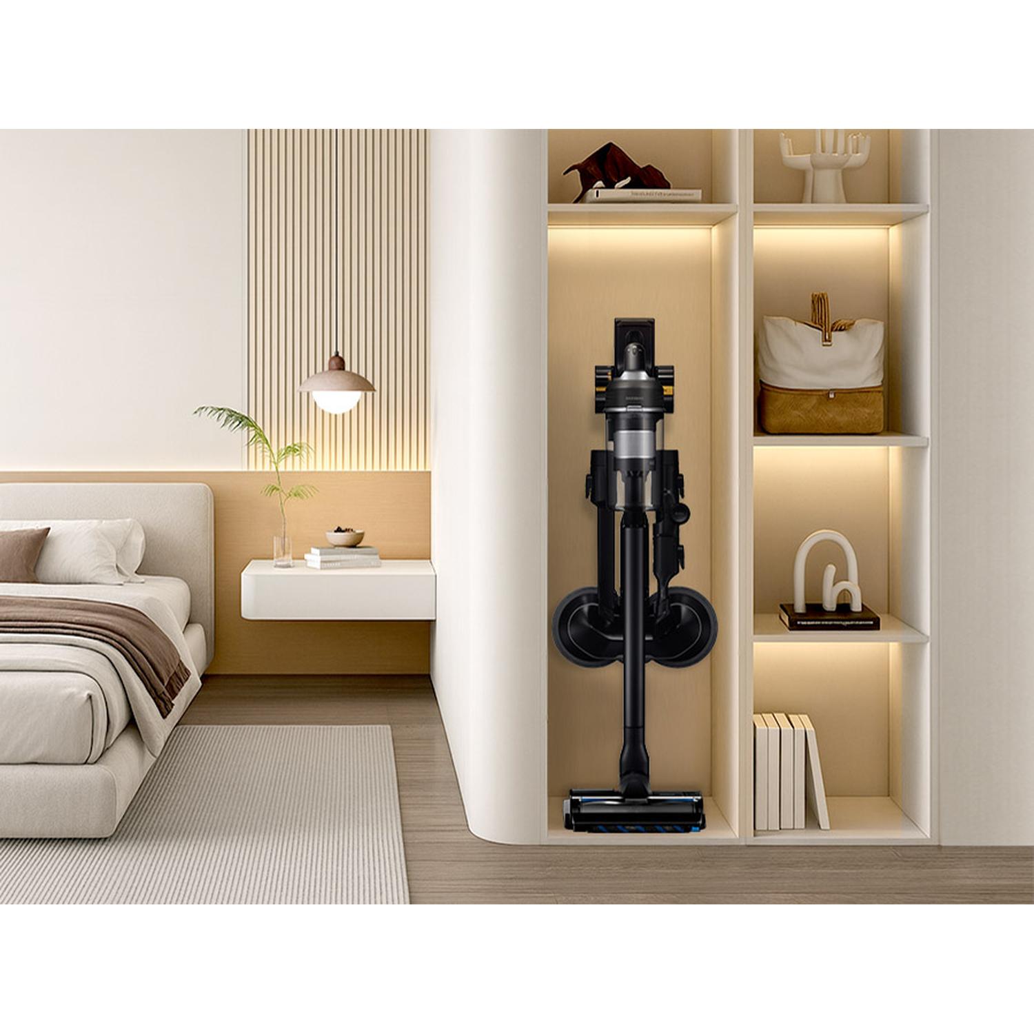 A black vacuum cleaner stands in a shelf next to a bed.