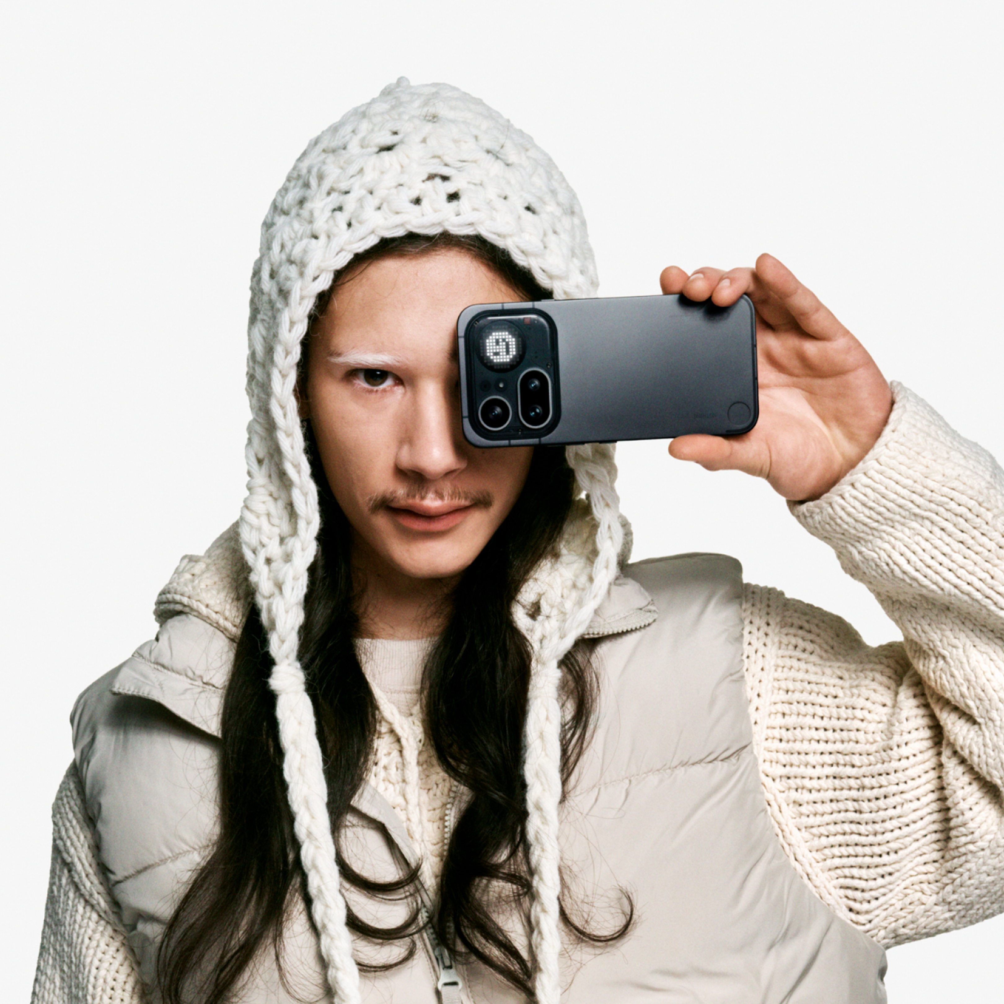 Mann mit Wollmütze hält ein Handy vor sein Auge.