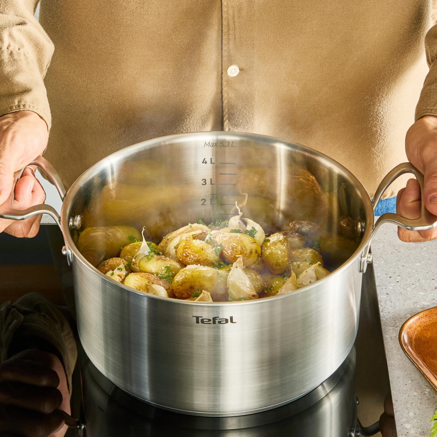 Een persoon houdt een dampende pan met aardappelen en knoflook vast.