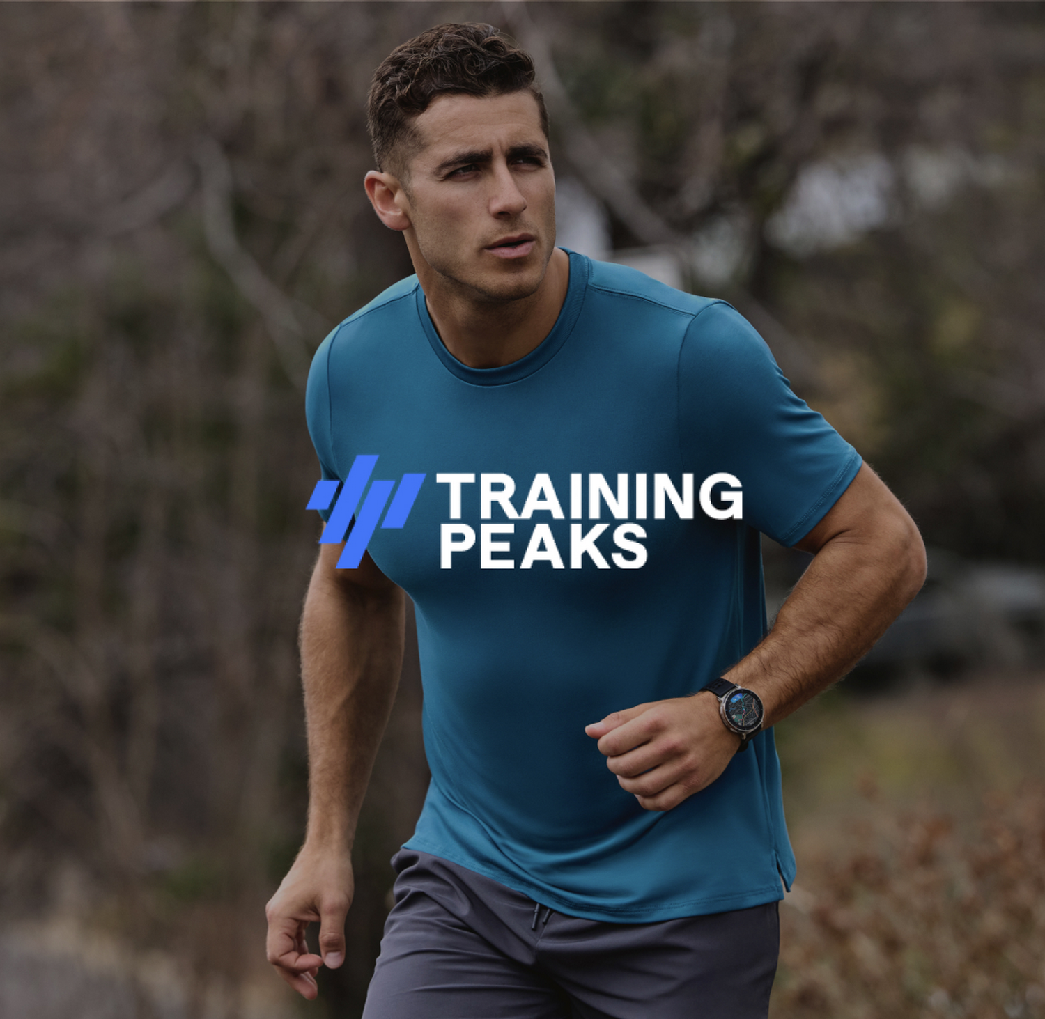 Un hombre con camiseta azul y pantalones cortos grises corre al aire libre. Logo Training Peaks.