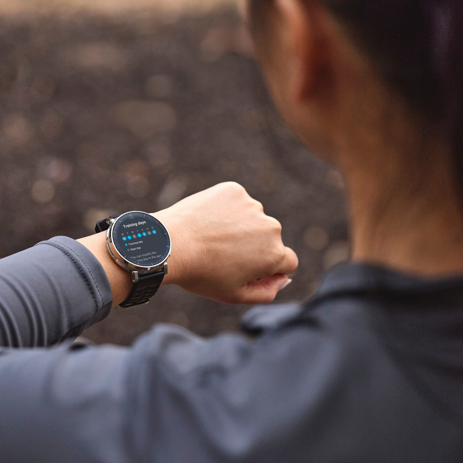 Una mujer con chaqueta gris mira su smartwatch con vista general de días de entrenamiento.