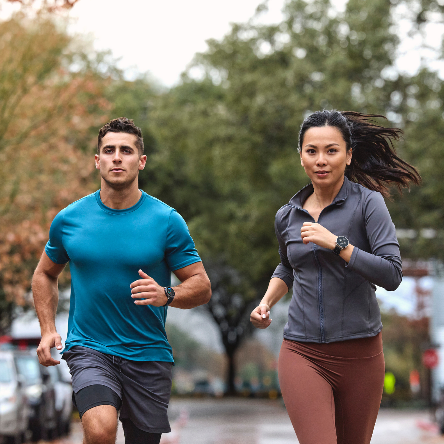 Hombre y mujer corriendo en una calle, árboles al fondo.