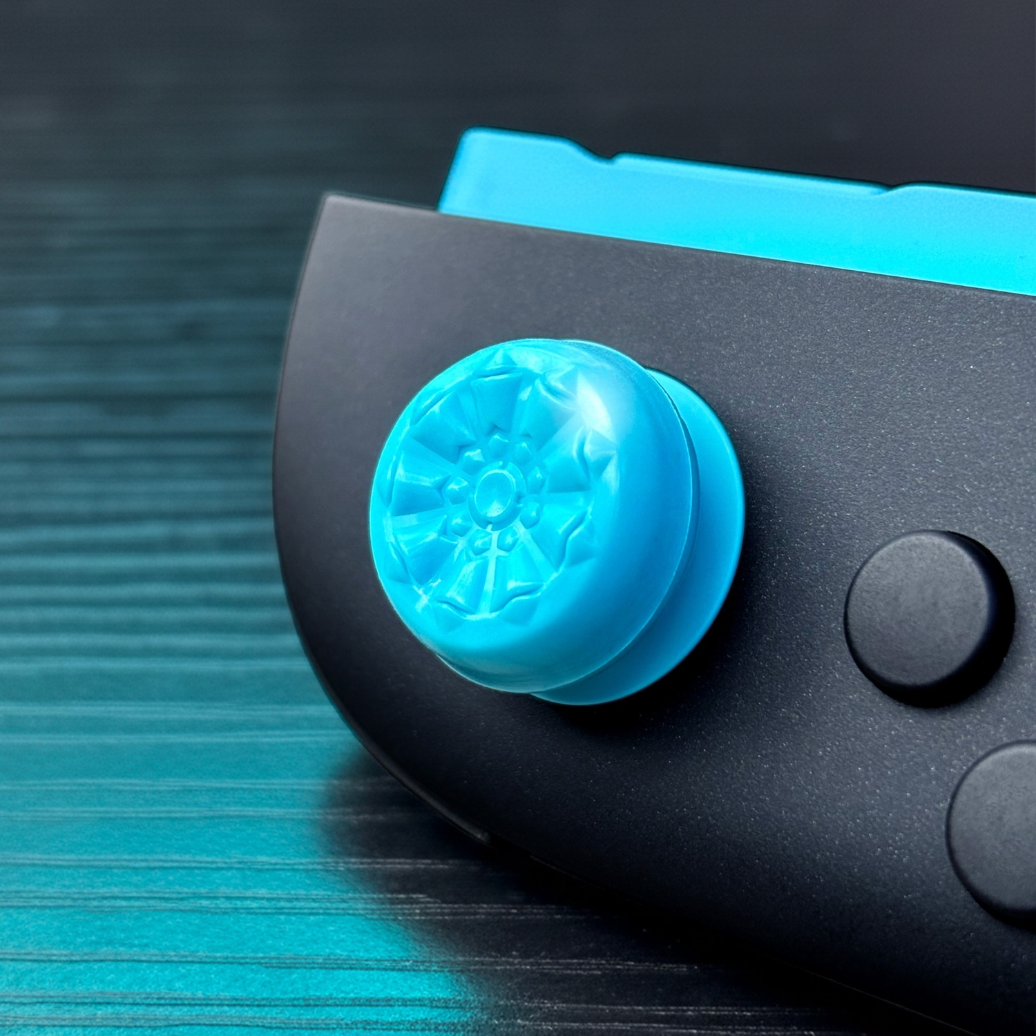 A blue joystick cap on a black controller with teal accents.
