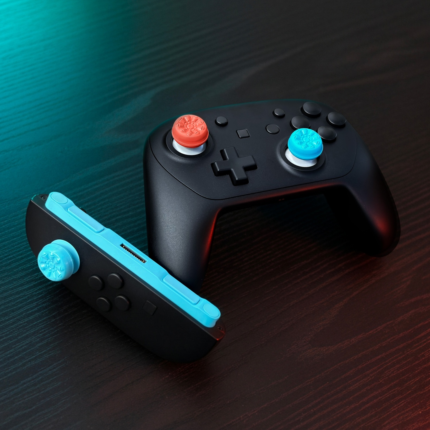 Two black game controllers on a wooden table. One has red, the other blue accents.