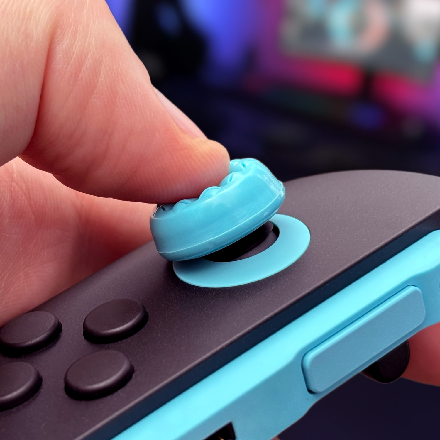 A thumb presses a blue joystick cap on a game controller.