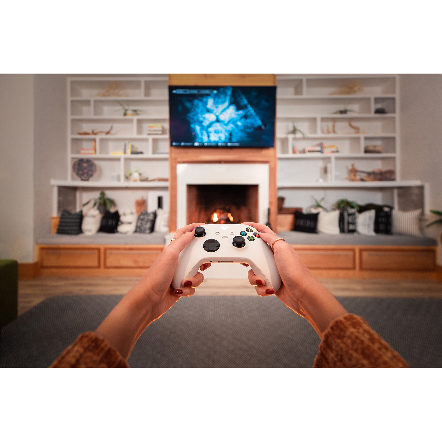 White controller hands holding a white Xbox controller in front of a fireplace.