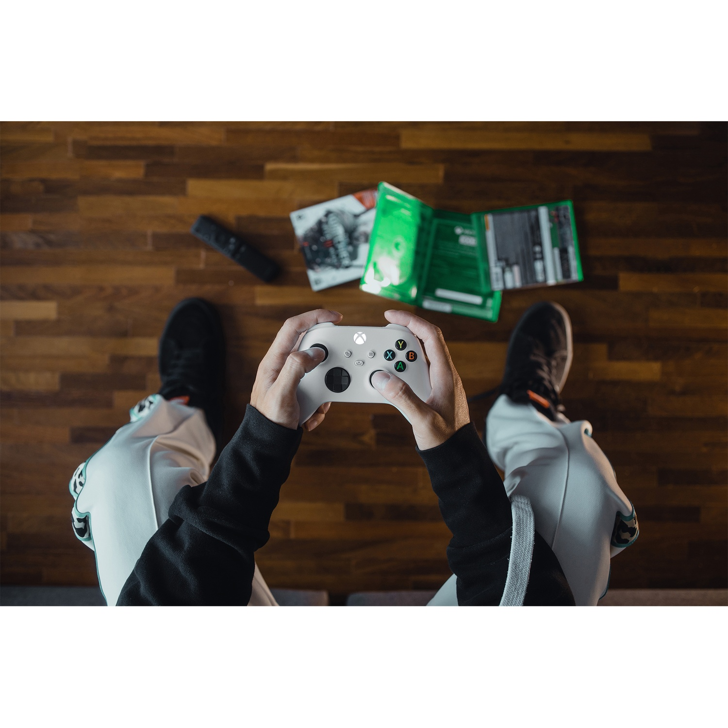 Personne tenant une manette blanche sur sol en bois, jeu et télécommande à proximité.