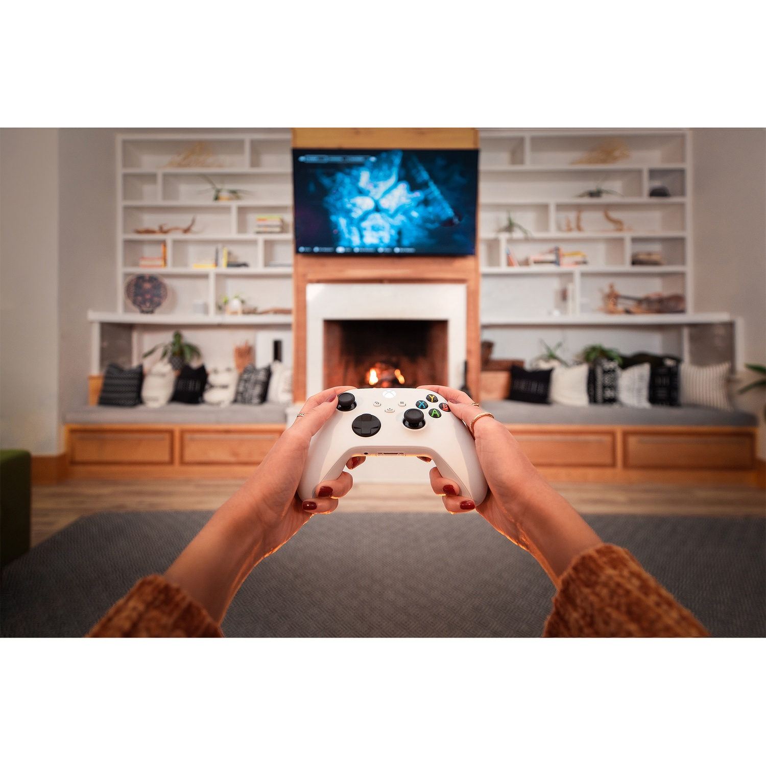 Mains tenant une manette blanche devant une cheminée et une télévision.