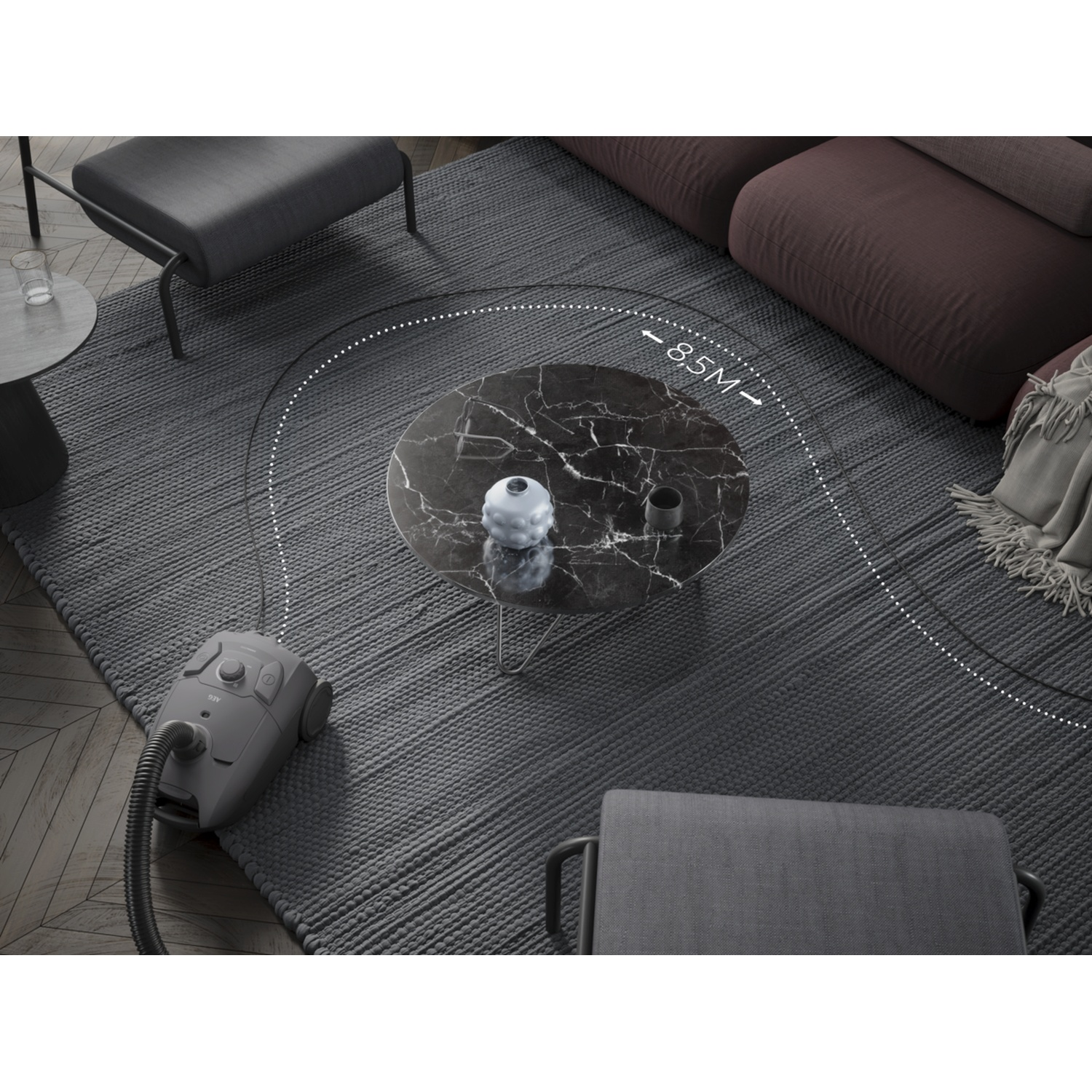 A grey vacuum cleaner on a rug in a living room, near a marble coffee table.