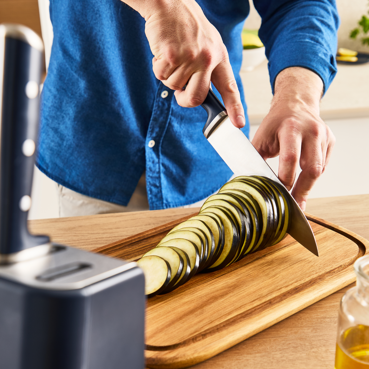 A person slices an eggplant on a wooden cutting board.