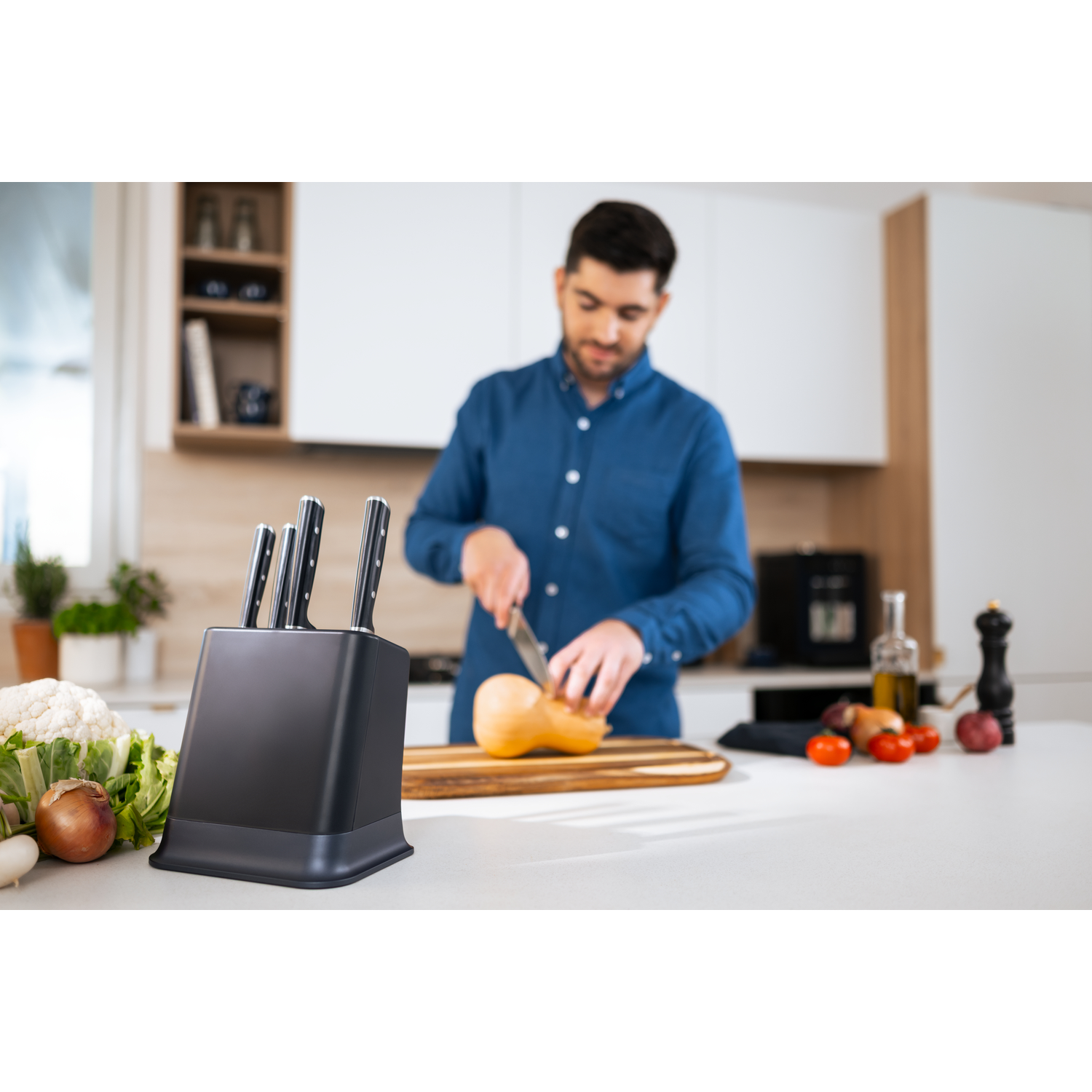 Man cutting butternut squash in a modern kitchen with vegetables and knife block.