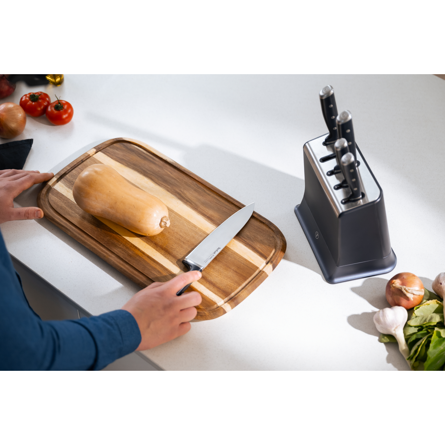 A butternut squash rests on a wooden board next to a knife block.