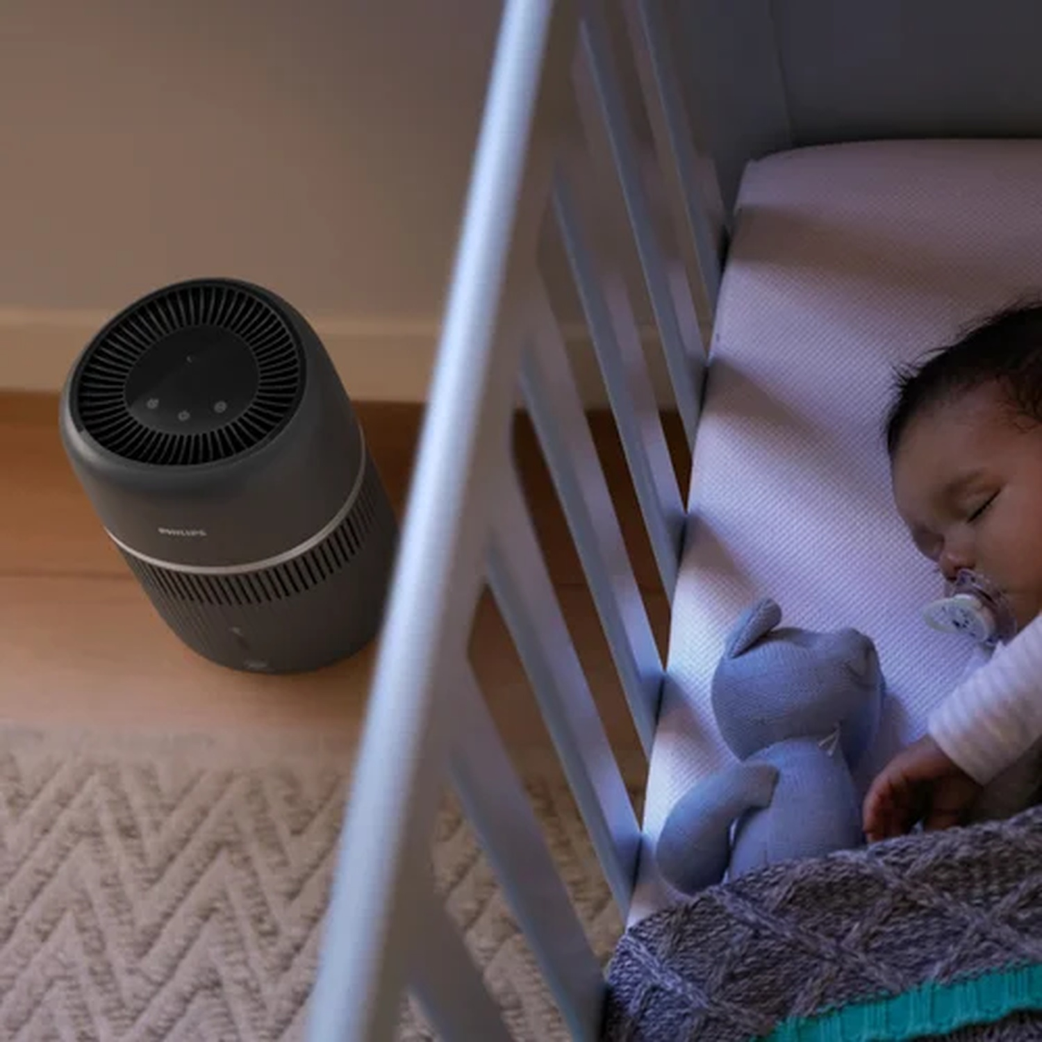 A baby sleeps in a crib next to an air purifier.