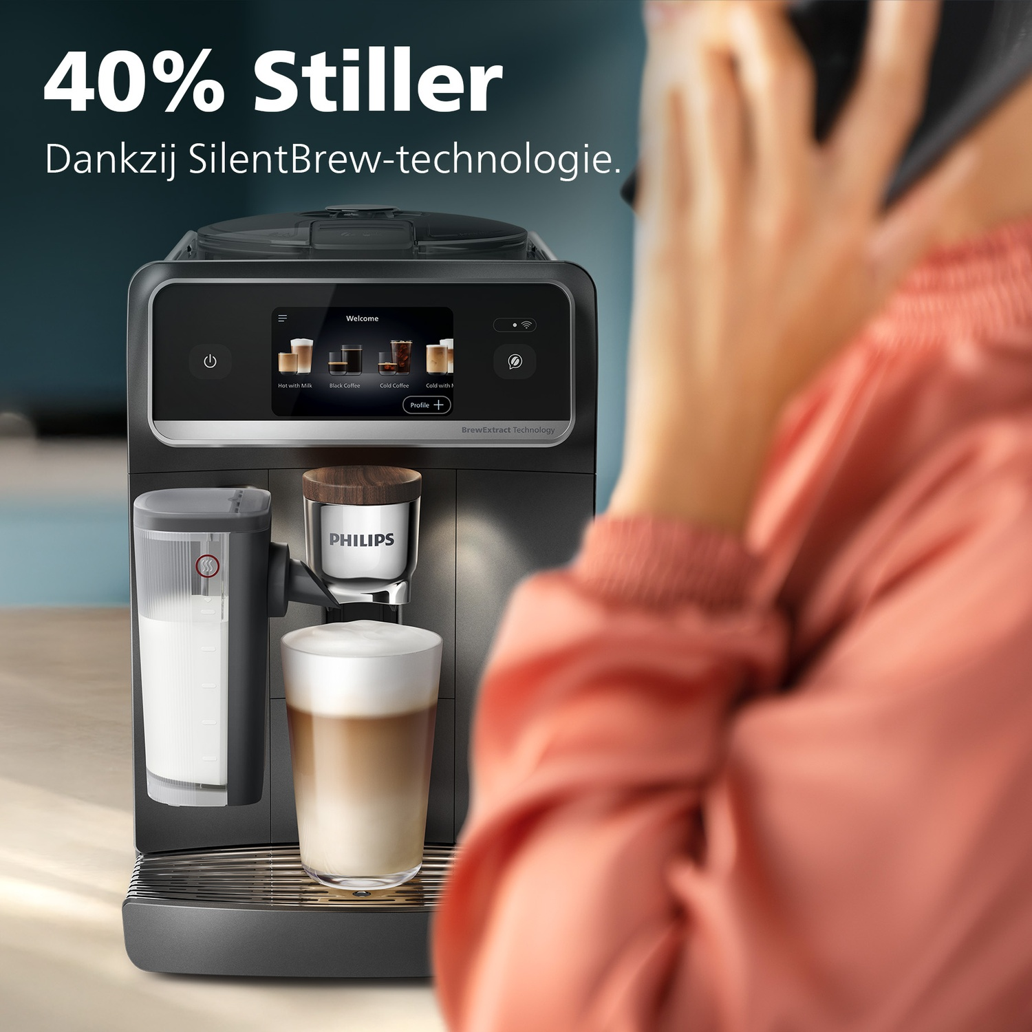 Coffee machine with milk carafe and glass of latte. Person on phone.