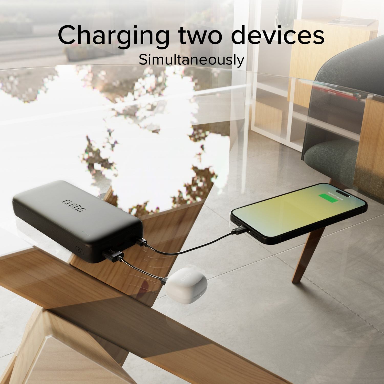 Batterie externe noire charge un smartphone et des écouteurs blancs sur une table en verre.