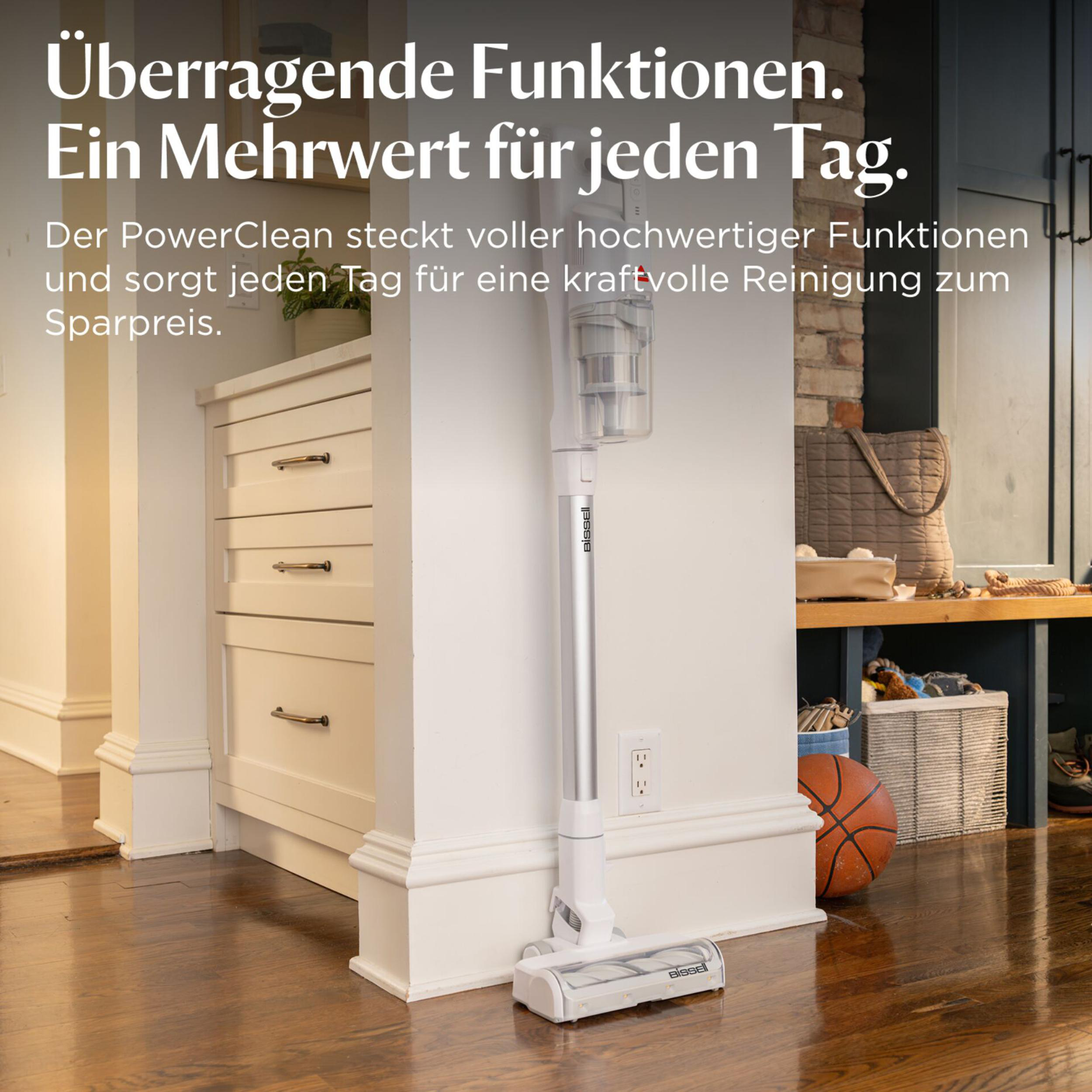 Ein weißer Akku-Staubsauger steht neben einer Kommode und einem Basketball.