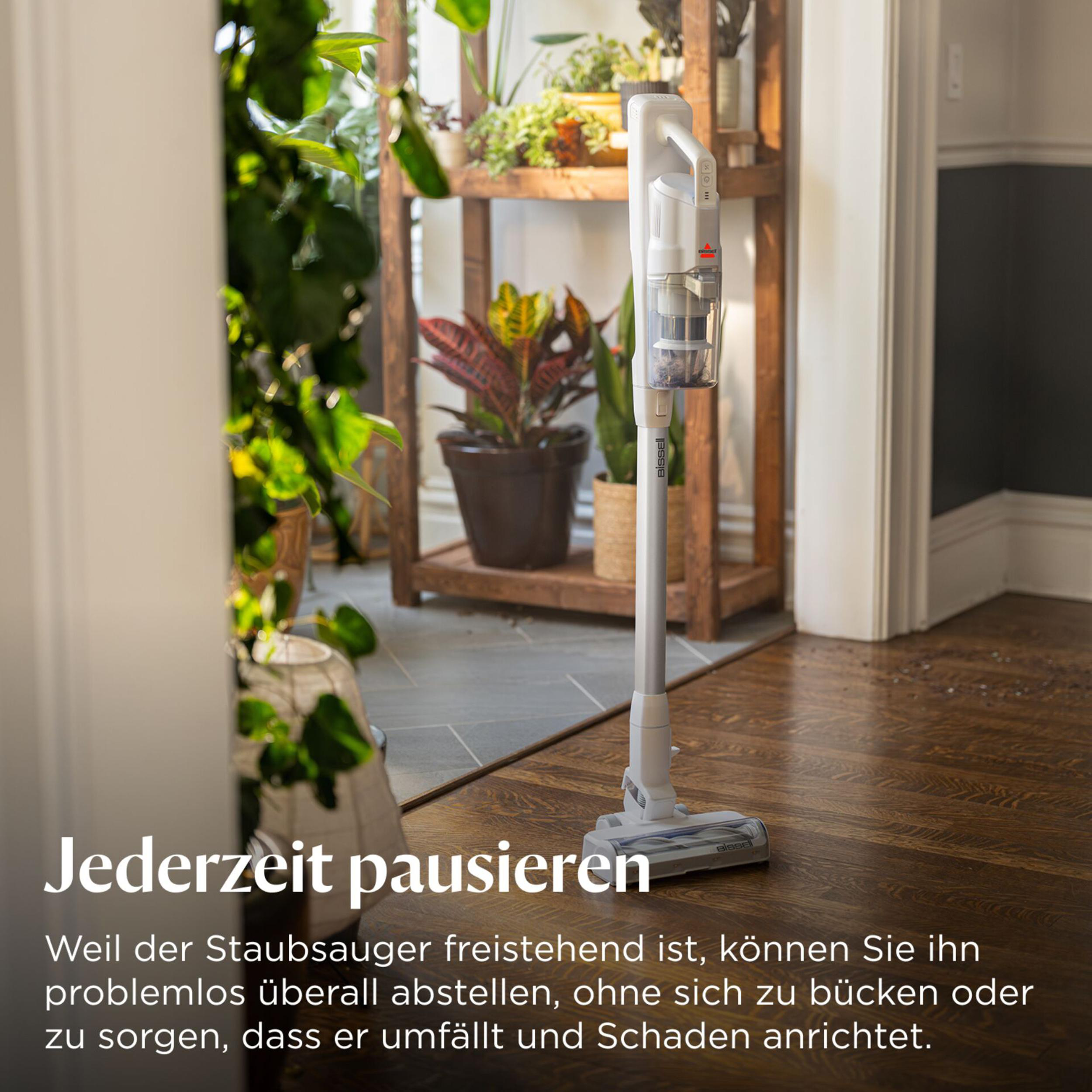 Ein weißer Staubsauger steht auf einem Holzboden vor Pflanzen.