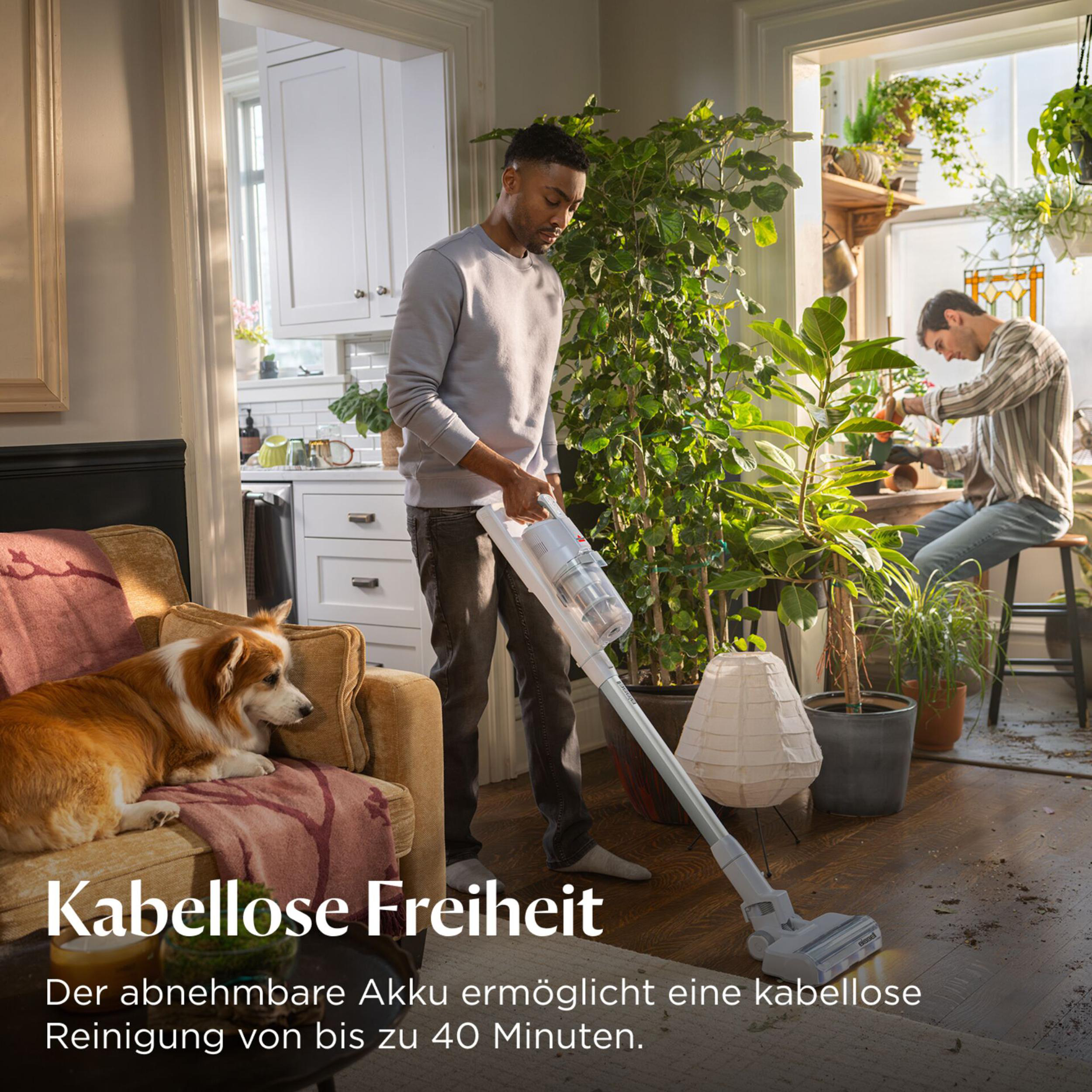 Ein Mann saugt einen Holzboden, ein Hund liegt auf einem Sessel.