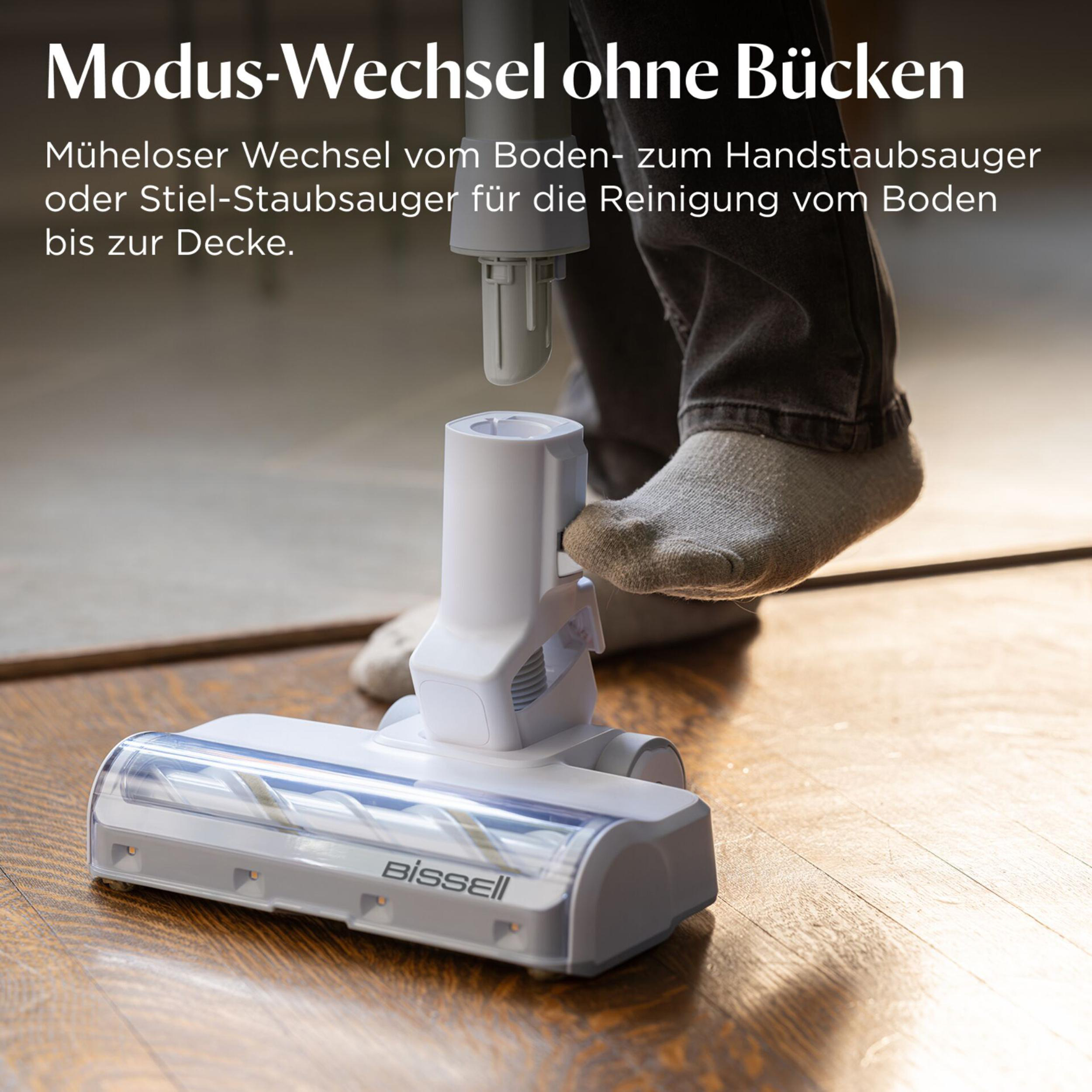 Ein weißer Bissell Staubsauger auf einem Holzboden, mit einem Fuß, der ihn bedient.