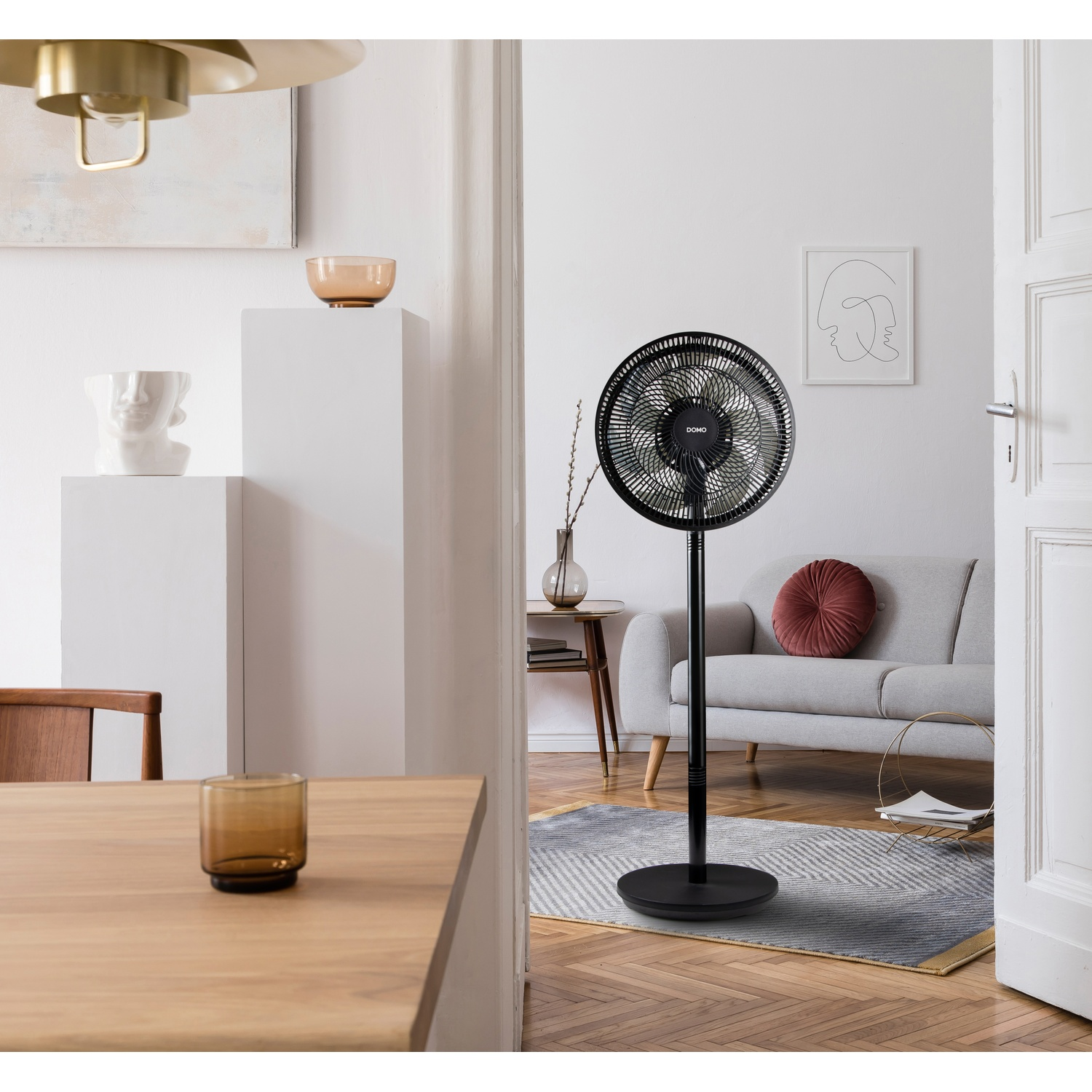 A black standing fan is next to a grey sofa with a round pillow.