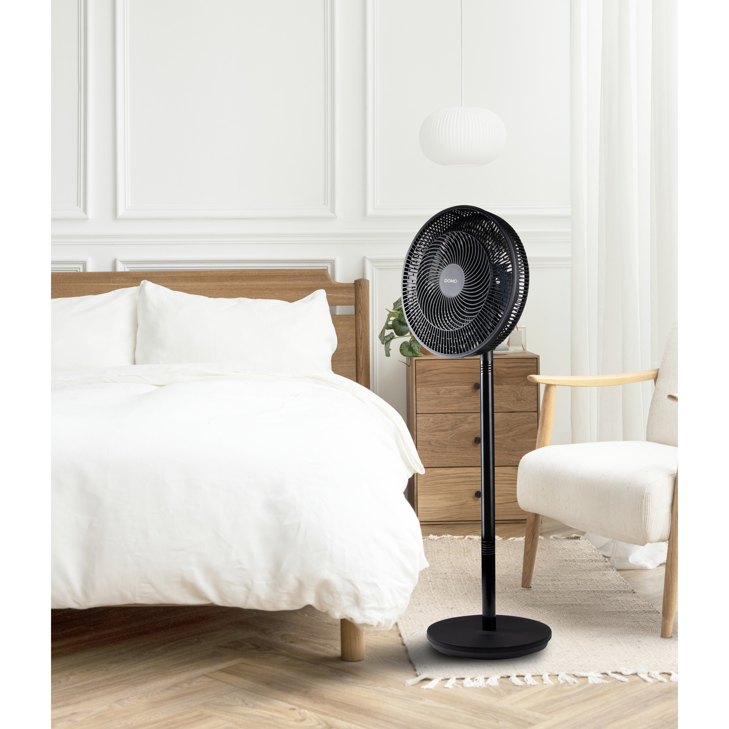 A black standing fan is positioned next to a bed in a bedroom setting.